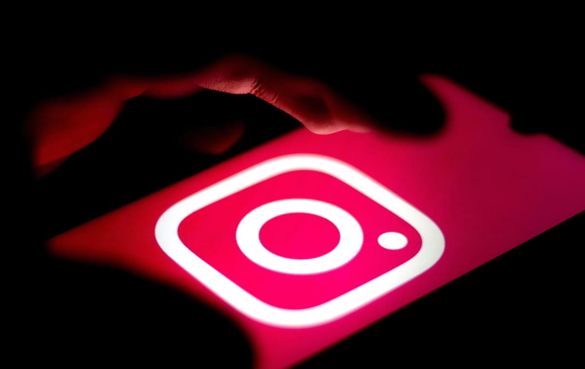 a photo of one hand using a smartphone with a logo of instagram on the screen.